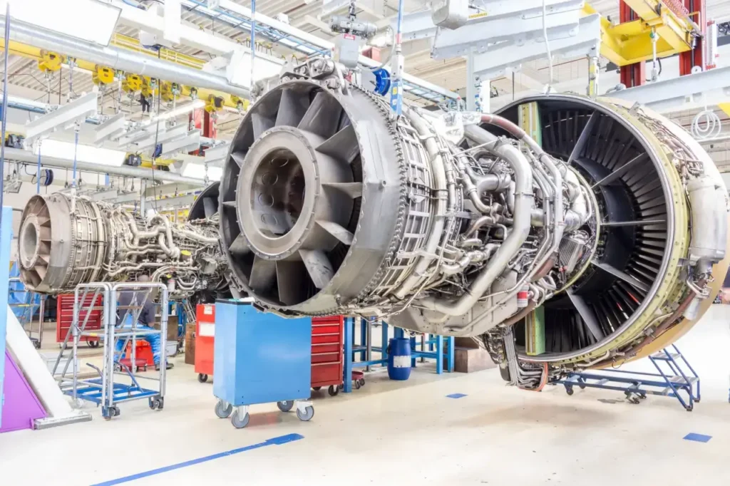 - RobotsInc.com Jet engine undergoing maintenance in an airplane overhaul hangar, with exposed turbines, piping, and maintenance carts nearby.