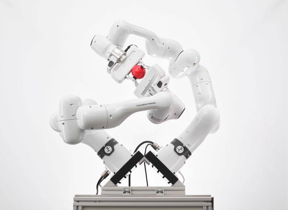 - RobotsInc.com Industrial robotic arm with multiple white segments mounting a gripper, positioned over a metal work surface (robotic automation setup)