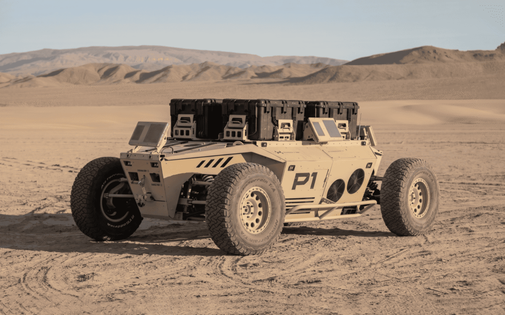 - RobotsInc.com Desert robotic rover labeled P1 with large tires and equipment on its rack in sandy terrain.
