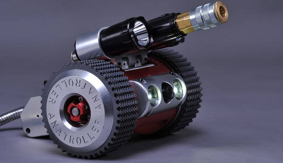 - RobotsInc.com Close-up of a compact mechanical device with a large toothed gear and a top-mounted brass connector on a gray background.