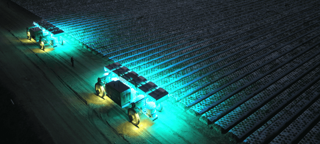 - RobotsInc.com Night scene of a turquoise-lit autonomous rover with solar panels traveling across a snow-covered field, leaving tracks behind.