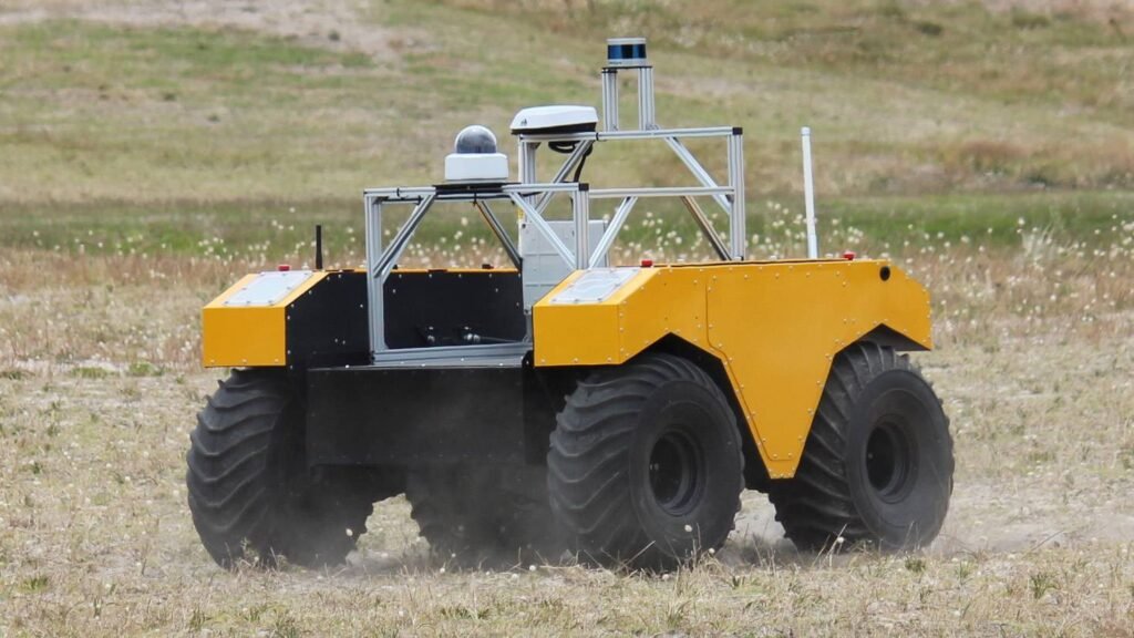 - RobotsInc.com Six-wheeled autonomous rover with a yellow body and exposed metallic frame driving across a dry field.