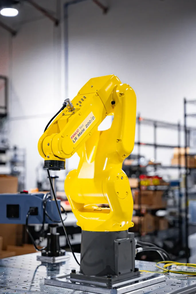 » RobotsInc.com Yellow industrial robotic arm mounted on a metal platform in a factory setting.