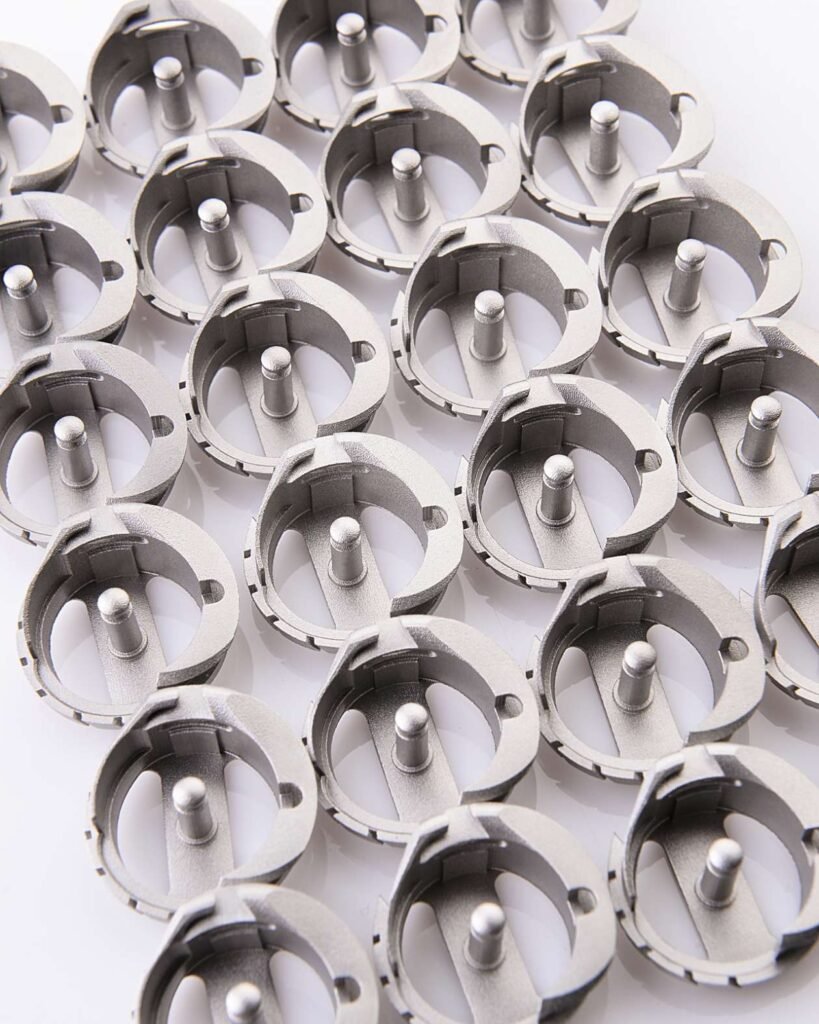 - RobotsInc.com Close-up of many identical silver circular mechanical parts with central pins arranged on a white surface.
