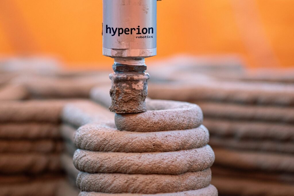 - RobotsInc.com Close-up of a silver cylinder labeled 'hyperion robotics' perched on stacked stones with an orange background.