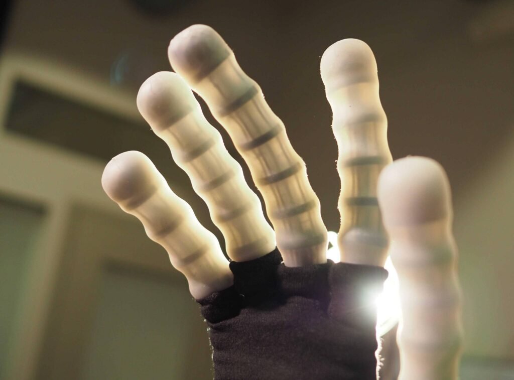 - RobotsInc.com Close-up of several translucent artificial fingers reaching upward, softly backlit to create a glowing effect.