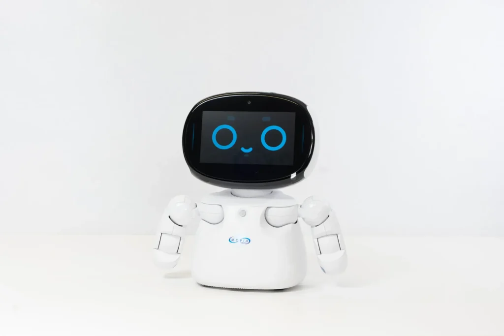 » RobotsInc.com White humanoid robot with a black screen head displaying a blue smiling eyes and mouth, centered on a white background.
