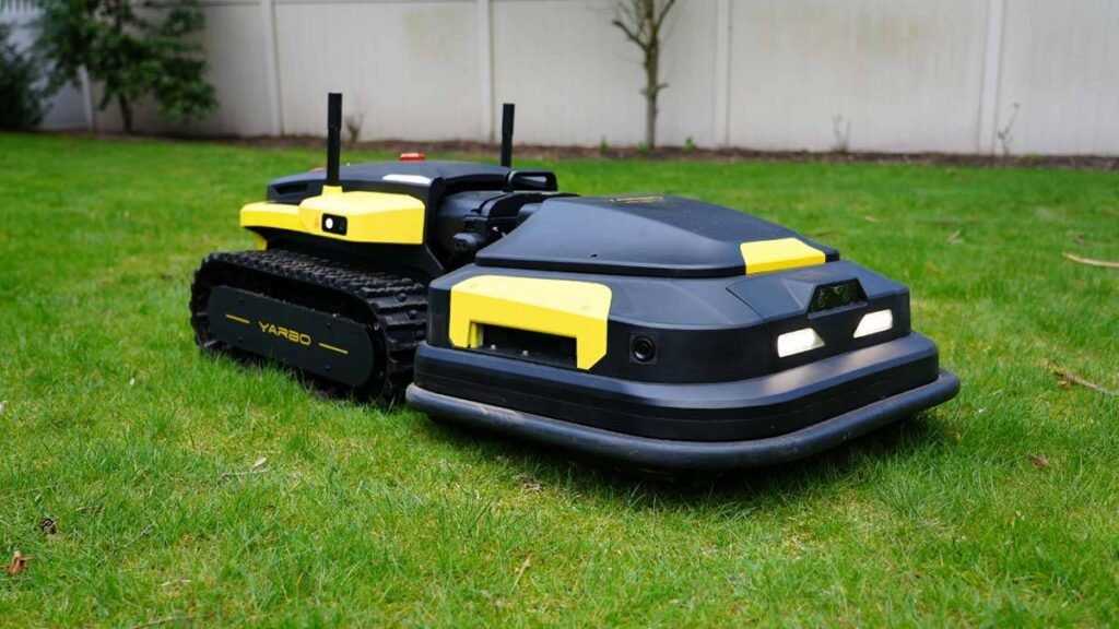 - RobotsInc.com Autonomous robotic lawn mower on a green lawn, black and yellow with track wheels on the left side landscaping the grass.